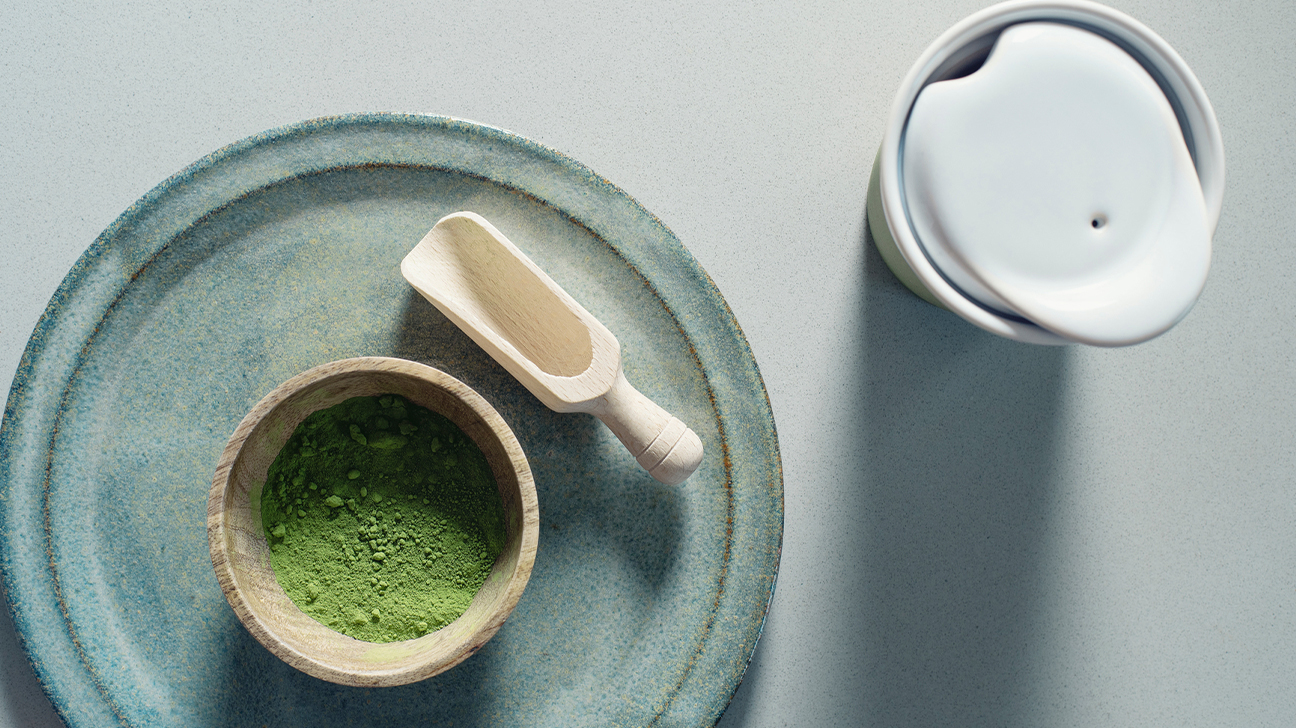 Matcha powder and a wooden spoon on blue plate.