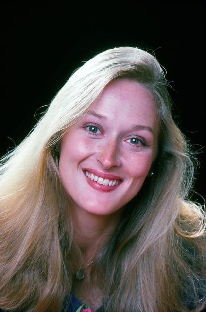 Young Meryl Streep smiling broadly at the camera with her long blonde hair framing her face.